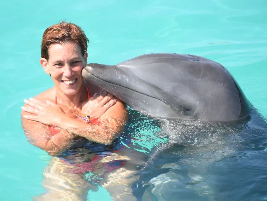 Manuela, sonriendo en el agua mientras un delfín la besa suavemente en el hombro.