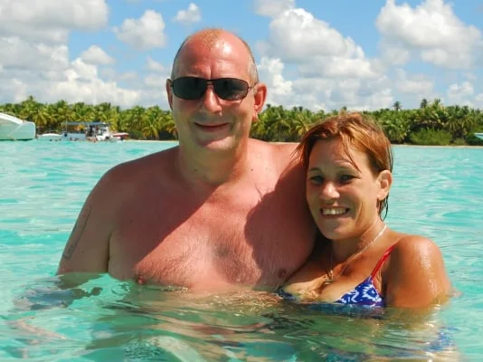 Manuela y Rainer, sonriendo en el agua clara y turquesa, con paisaje tropical al fondo.